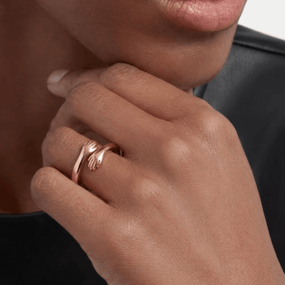 Close-up of a rose gold adjustable hug ring with small hands design on a moans hand