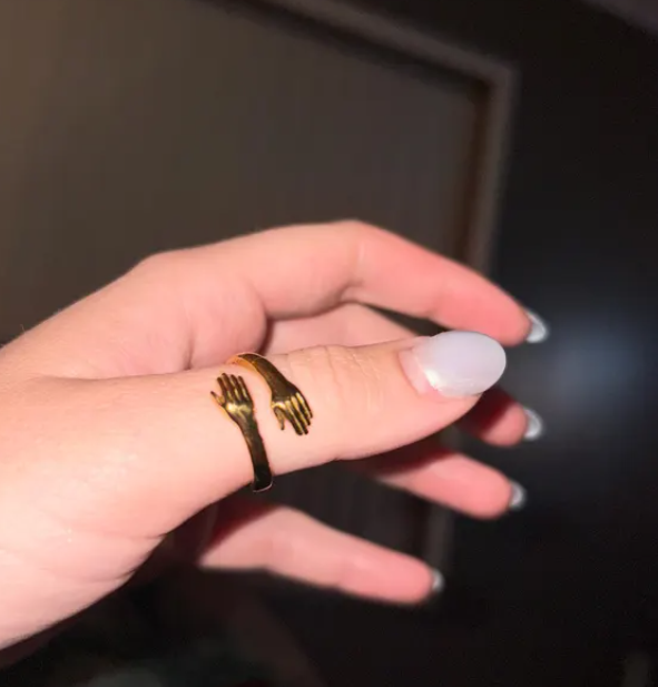 Gold hug ring with small hands design, adjustable, shown on a woman's finger