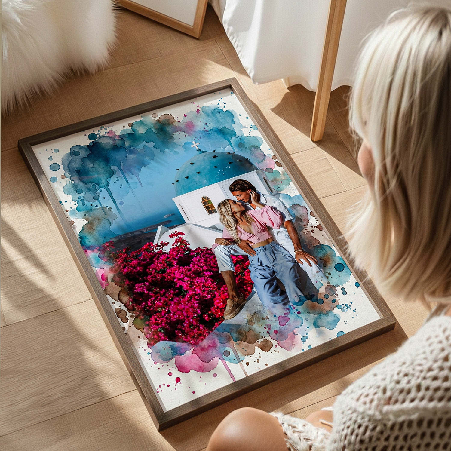 Personalized watercolor canvas of a couple embracing with a white village background, featuring blue and gray paint splatters, leaning against a white wall on a wood floor.