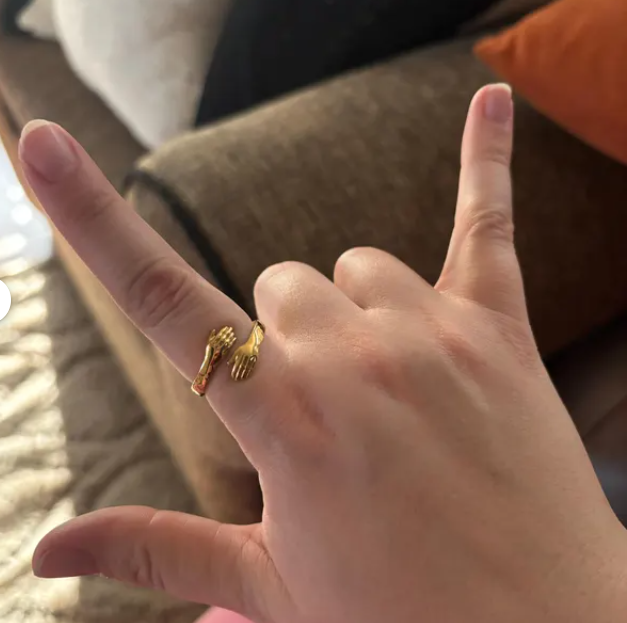 Close-up of a gold adjustable hug ring with small hands design on woman's finger