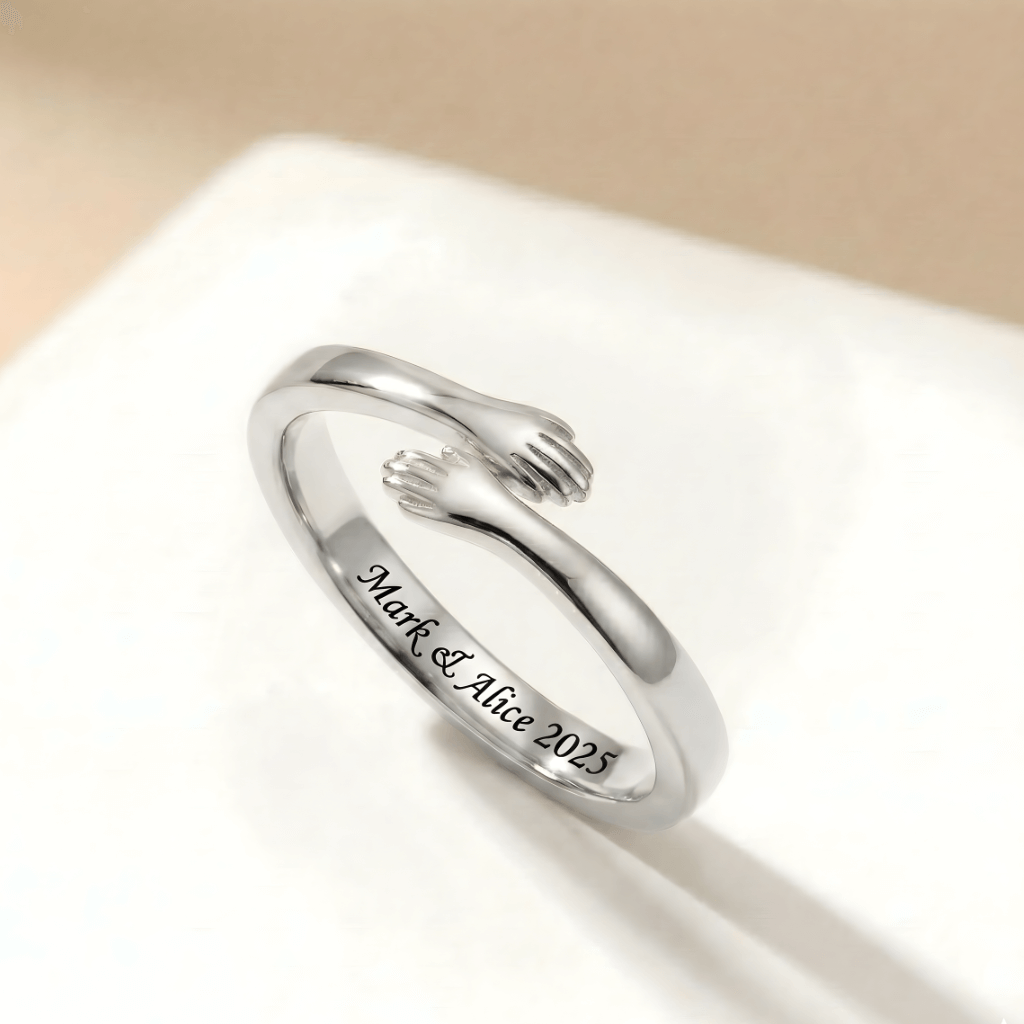 Close-up of a silver adjustable hug ring with small hands design, engraved with "Mark & Alice 2025