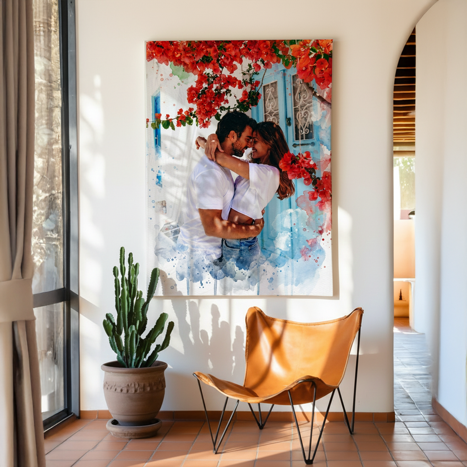 Large personalized canvas of a couple embracing in front of a blue door and red flowers, with blue watercolor accents, displayed above a leather butterfly chair.