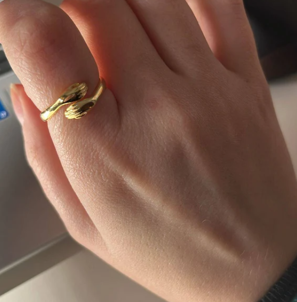 Close-up of a woman's finger wearing a gold hug ring shaped like small hands