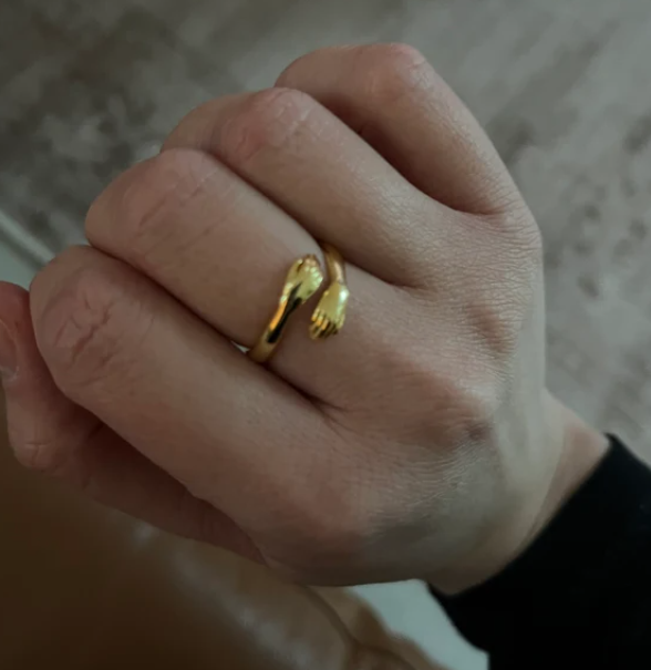 Gold adjustable hug ring featuring small hands, worn on a woman's finger, close-up
