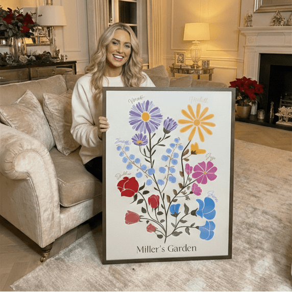 woman sitting on a chair holding a framed illustrated family garden 