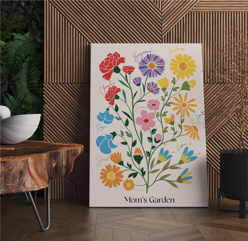 A "Mom's Garden" birth flower wrapped canvas print leaning against a slatted wood wall in a modern room with a decorative table and plant.