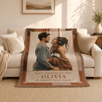 Personalized birthday woven blanket in the Birthday Love terracotta design on a sofa, with a woven birthday message and name