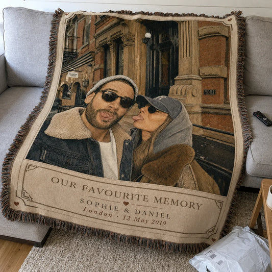 Custom couple woven blanket in the Favourite Memory design draped on a sofa — vintage postcard frame with names, place and date
