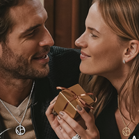 Couple smiling at eachother while wearing matching monogram necklace while holding gift box 