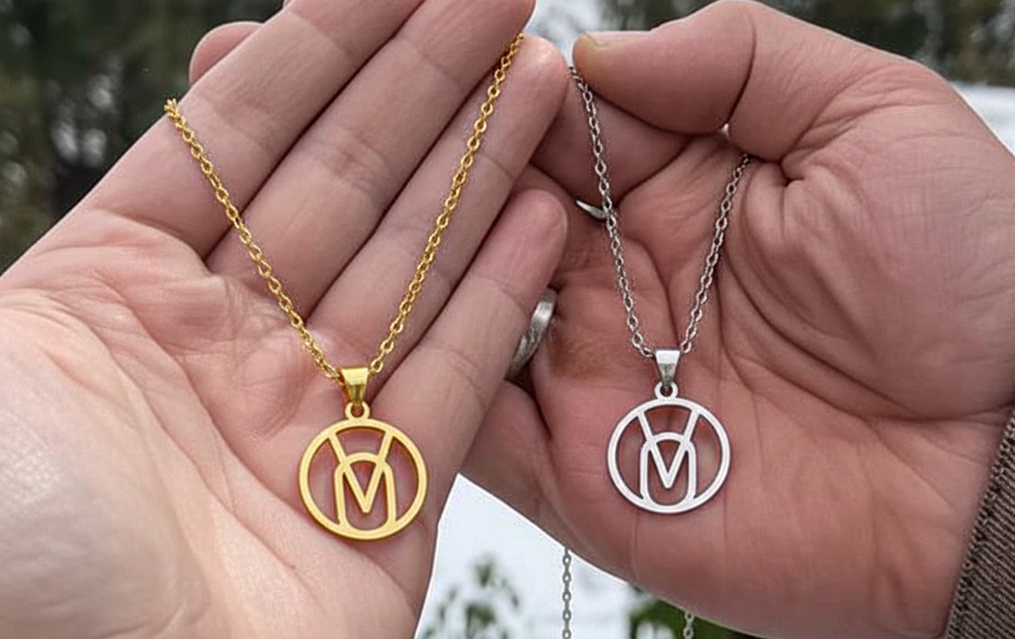 couple holding matching monogram necklaces in gold and silver