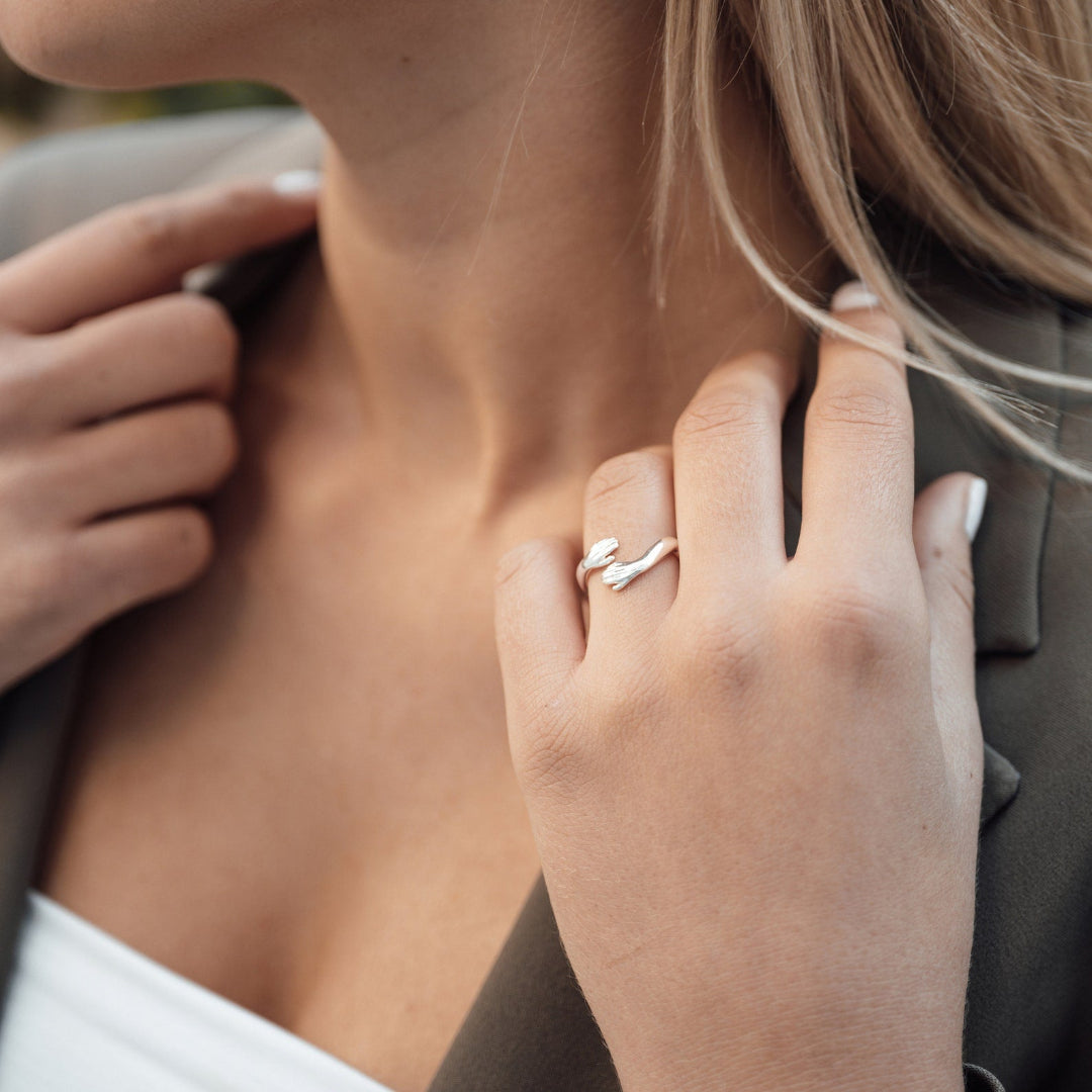 Silver adjustable hug ring with hand motif, shown on a woman's finger