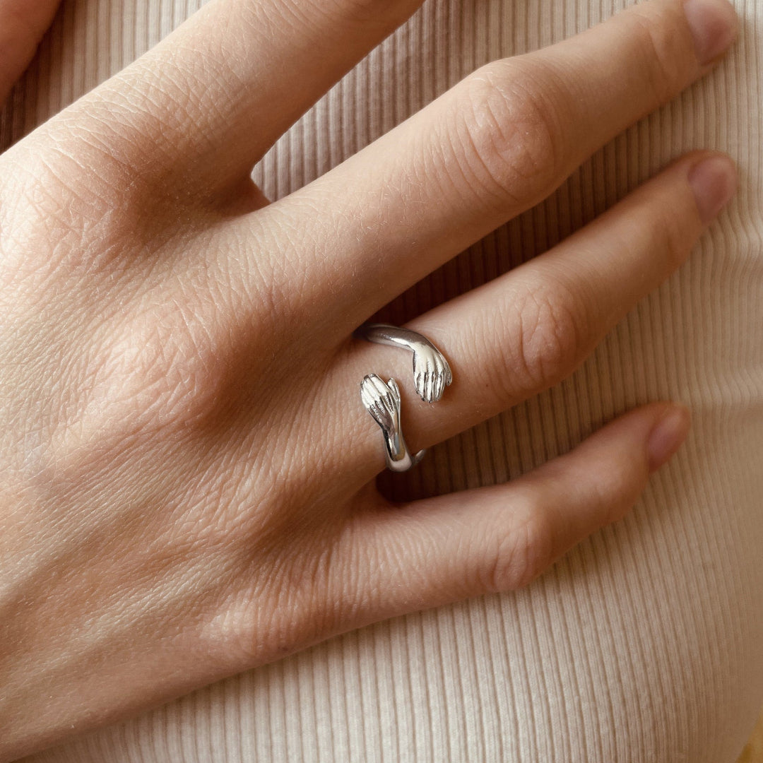 Gold hug ring with tiny hands design, adjustable, on a woman’s finger