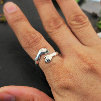 Close-up of an adjustable silver ring with small hands hugging the finger