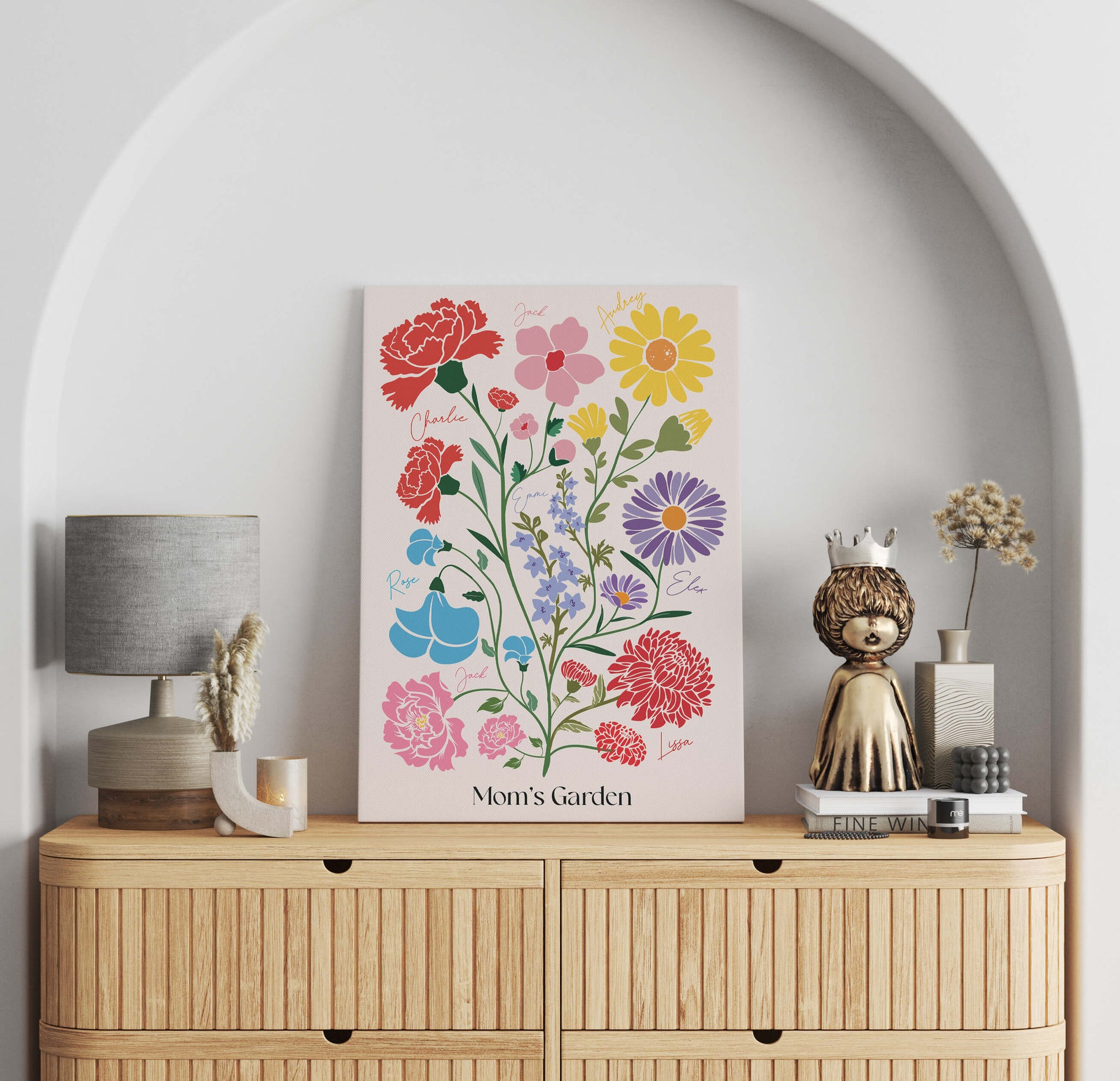 A framed "Mom's Garden" birth flower art piece displayed on a wooden dresser alongside a lamp and decorative gold figurine.
