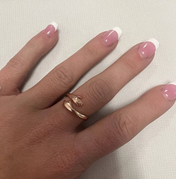 Close-up of rose gold hug ring featuring miniature hands hugging the finger