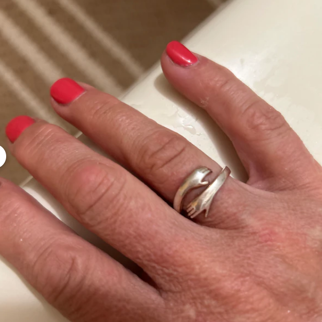 Detail shot of a silver adjustable ring in the shape of tiny hands on a woman's finger